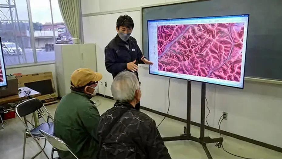 境界確認の様子：屋内で大型モニターに映し出された森林の航空レーザー測量図（赤色立体地図）を見ながら、担当者が所有者に境界の位置を説明している風景
